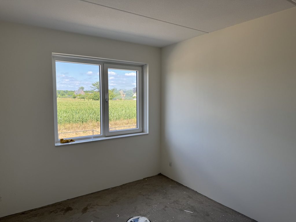 Lege nieuwbouwslaapkamer met gladde lichte wanden en uitzicht over een maisveld