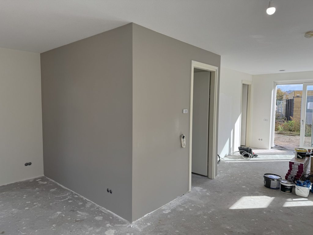 Nieuwbouwwoning met een pas afgewerkte grijze wand en verfemmers op de betonvloer
